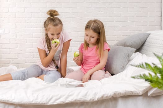 two cute children girls use digital tablet in bed. child playing on tablet pc.