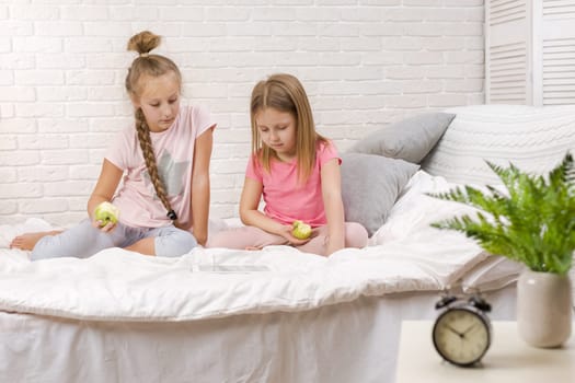two cute children girls use digital tablet in bed. child playing on tablet pc.