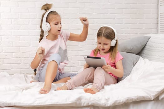 two cute children girls playing in the bedroom. two cute children girls use digital tablet in bed.