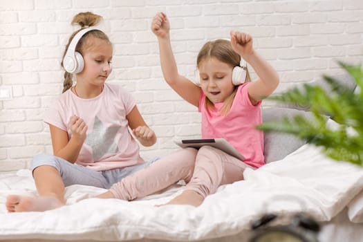 two cute children girls playing in the bedroom. two cute children girls use digital tablet in bed.