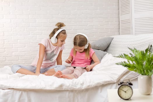 two cute children girls playing in the bedroom. two cute children girls use digital tablet in bed.