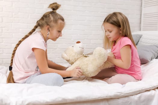 two cute children girls playing doctor with teddy bear at home. girl listens a stethoscope to toy.