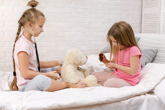 two cute children girls playing doctor with teddy bear at home. girl listens a stethoscope to toy.