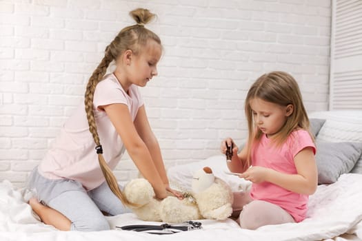 two cute children girls playing doctor with teddy bear at home. girl listens a stethoscope to toy.