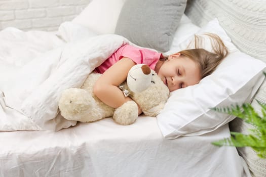 Cute little child girl sleeping with teddy bear in her bed
