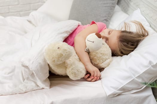 Cute little child girl sleeping with teddy bear in her bed