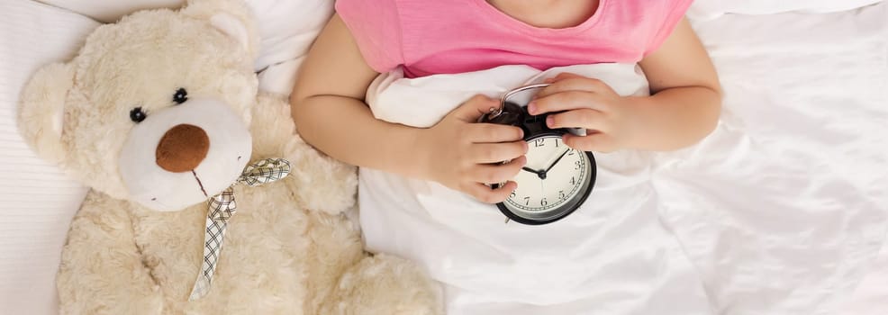 close-up, little child girl with clock in bed. good morning