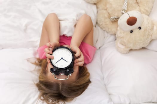 cute little child girl in pyjamas with clock in bed. good morning. top view