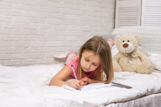 cute little girl drawing pictures while lying on bed. Kid painting at home