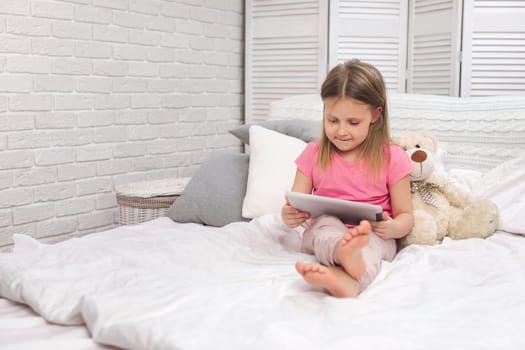 cute little child girl lies in bed uses digital tablet. child playing on tablet pc.