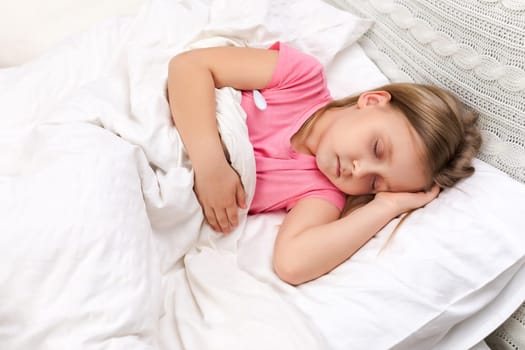 Sick little child girl lying in bed with thermometer. Cold flu season