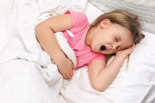 Sick little child girl lying in bed with thermometer. Cold flu season