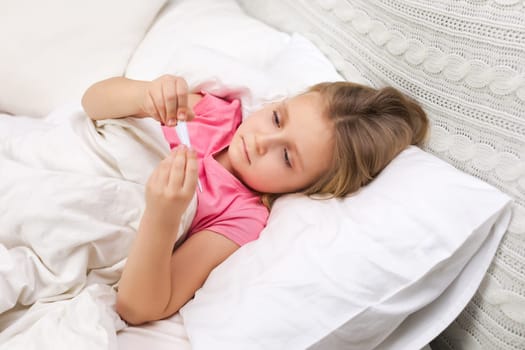Sick little child girl lying in bed with thermometer. Cold flu season