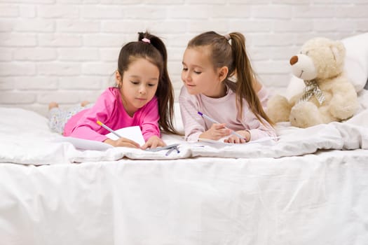 kids drawing pictures while lying on bed. pajama party and friendship.