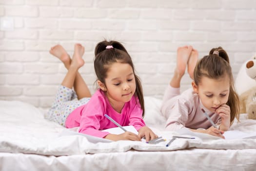 kids drawing pictures while lying on bed. pajama party and friendship.