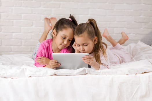 two cute children girls use digital tablet in bed. child playing on tablet pc.