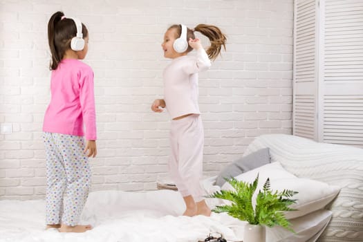 little children girls listening to the music with the headphones and dancing on bed. pajama party and friendship.