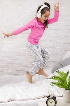 little child baby girl listening to the music with the headphones and dancing on bed. happy morning