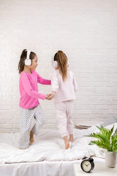 little children girls listening to the music with the headphones and dancing on bed. pajama party and friendship.