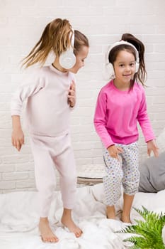 little children girls listening to the music with the headphones and dancing on bed. pajama party and friendship.