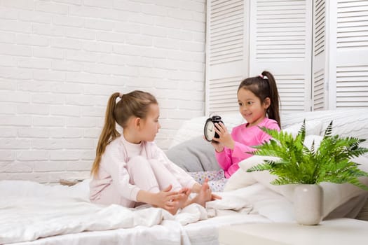 two cute children girls with clock in bed in the morning
