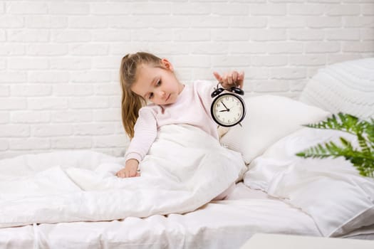 cute little child girl in pyjamas with clock in bed. good morning