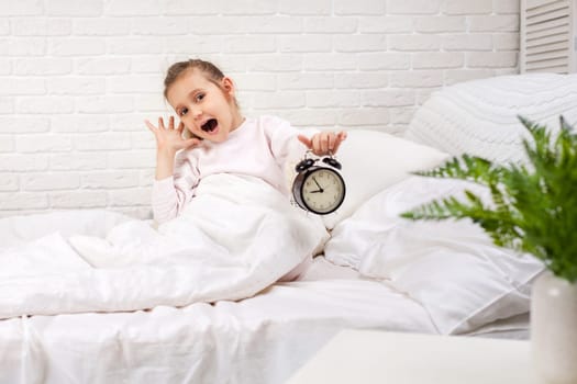 surprised little child girl in pyjamas with clock in bed. good morning