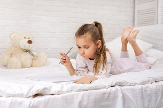 cute little girl drawing pictures while lying on bed. Kid painting at home