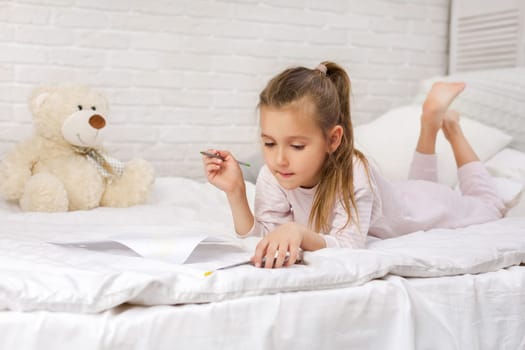 cute little girl drawing pictures while lying on bed. Kid painting at home