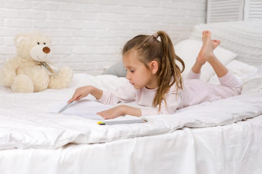 cute little girl drawing pictures while lying on bed. Kid painting at home