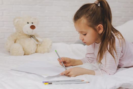 cute little girl drawing pictures while lying on bed. Kid painting at home