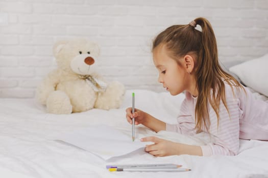 cute little girl drawing pictures while lying on bed. Kid painting at home