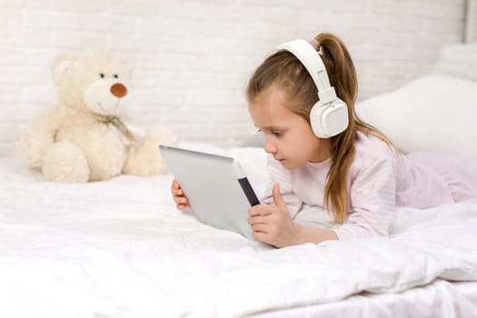 cute little child girl lies in bed uses digital tablet. child playing on tablet pc.