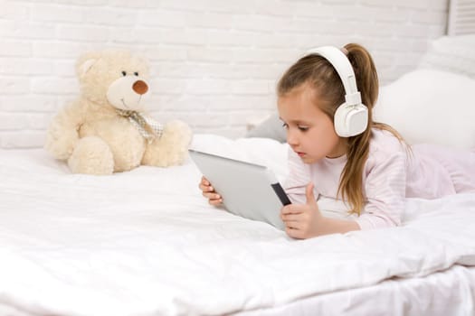 cute little child girl lies in bed uses digital tablet. child playing on tablet pc.