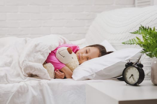Cute little child girl sleeping with teddy bear in her bed