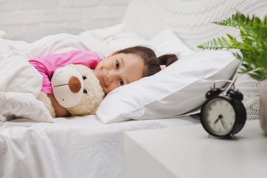 Cute happy little child girl sleeping with teddy bear in her bed