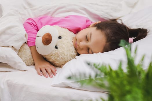 Cute little child girl sleeping with teddy bear in her bed