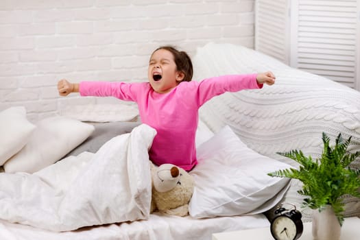 cute little child girl wakes up from sleep and yawns in bed in the morning