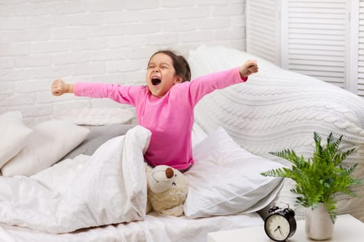 cute little child girl wakes up from sleep and yawns in bed in the morning