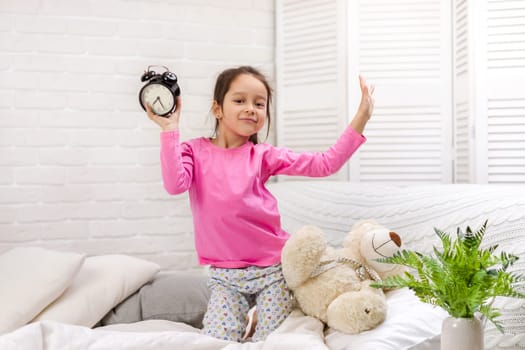 happy little child girl in pyjamas with clock in bed. good morning