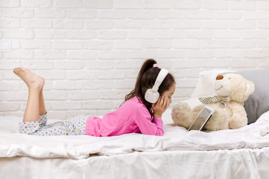 cute little child girl lies in bed uses digital tablet. child playing on tablet pc.