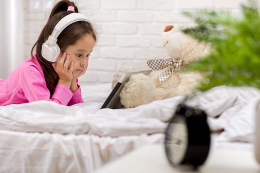 cute little child girl lies in bed uses digital tablet. child playing on tablet pc.