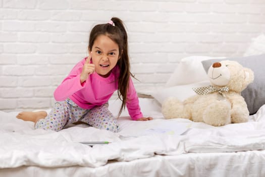 adorable little multinational child girl playing with teddy bear in bed in morning