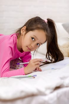 cute little girl drawing pictures while lying on bed. Kid painting at home