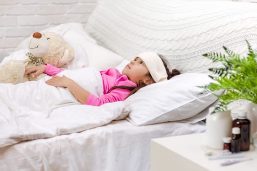 Sick little child girl lying in bed with thermometer. Cold flu season