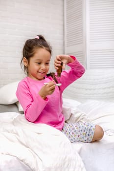 Sick little child girl pouring antipyretic syrup for kid in bed