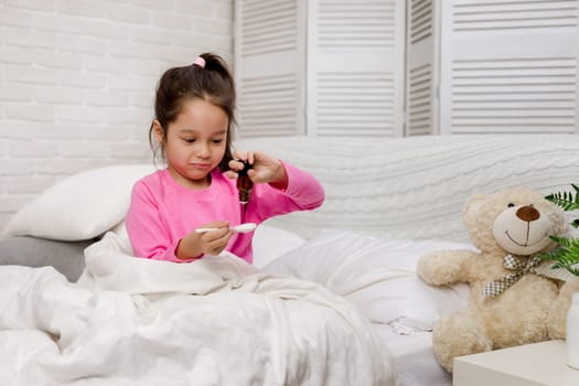 Sick little child girl pouring antipyretic syrup for kid in bed