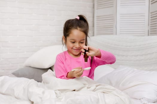 Sick little child girl pouring antipyretic syrup for kid in bed
