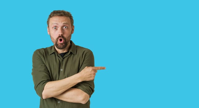 Surprise and excitement, man pointing arrow with hand aside to empty copy space on blue background. Attention to area of interest, making it ideal for use in advertising, promotions, or announcements. High quality photo
