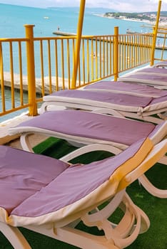 Free deck chairs stand in a row, empty beach chairs are waiting for tourists, vertical photo.